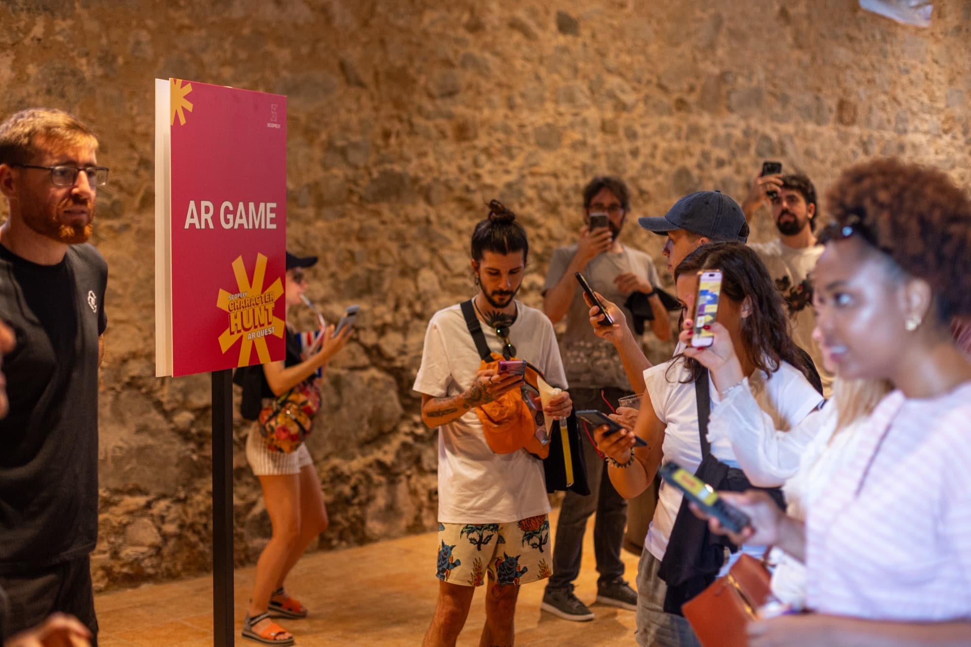Group indoors beside an AR GAME Scopely Character Hunt AR Quest sign, several holding phones.
