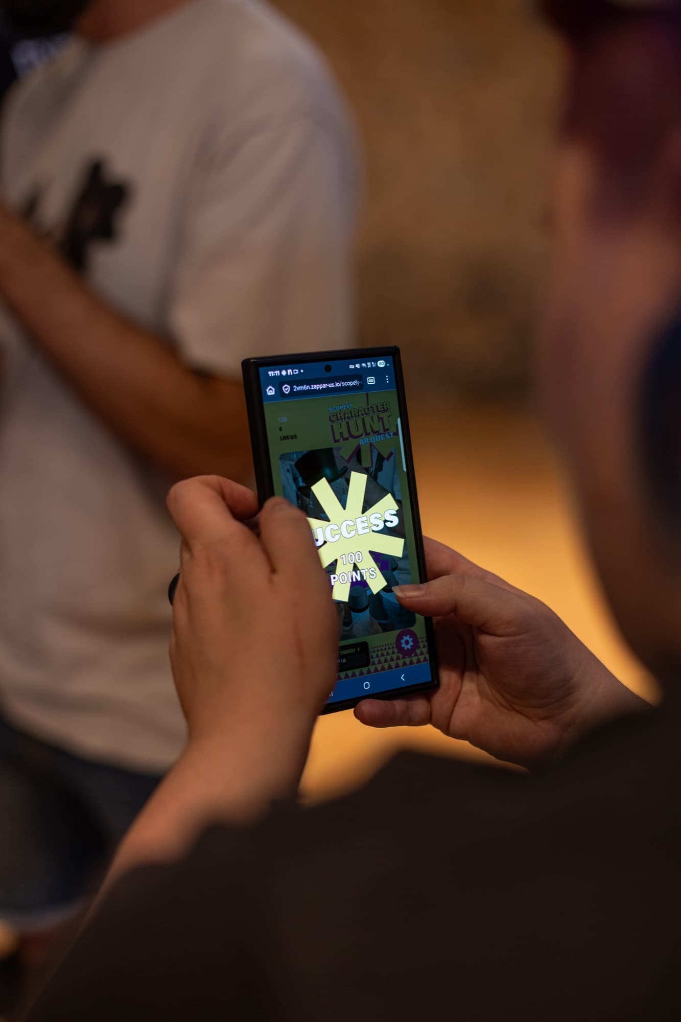 Hands holding a phone with a SUCCESS and 100 points overlay in the Character Hunt AR quest.